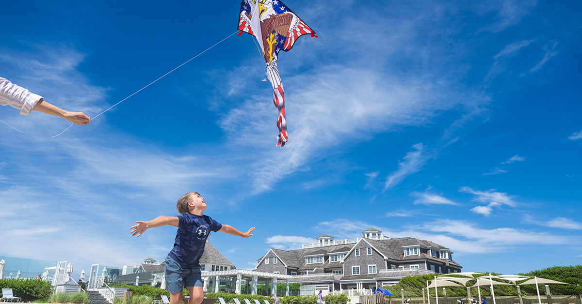 Child flying a kite on a sandy beach near a coastal clubhouse