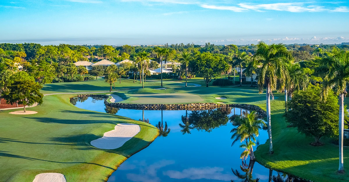 Scenic golf course with water hazard, sand bunkers, and palm trees under blue sky